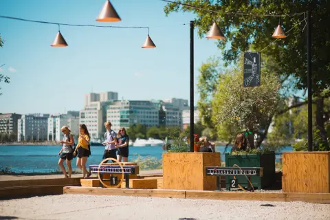 Vänner njuter av utomhusaktiviteter i Stockholm vid vattnet, med spel och stadens silhuett i bakgrunden.