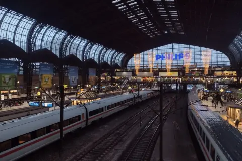 Tågstation med flera spår och vita tåg. En stor glas- och stålkonstruktion täcker taket. Philips-logotypen lyser i blått. Det är ett sj tåg till Hamburg.
