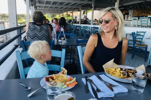 Familj njuter av en måltid på Costas Kitchen Kallithea. En kvinna ler, en pojke äter, och maten ser utsökt ut.