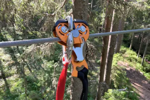 Nära en zipline i Umeå, en orange vajerklämma med röda och svarta band hänger redo för äventyr i skogen.