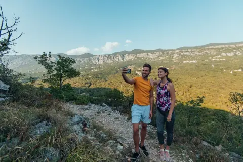 Ett par tar en selfie under sin vandring i Kroatien, med en fantastisk utsikt över berg och grönska.