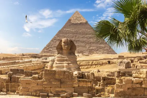 Den ikoniska Sfinxen och pyramiderna i Egypten, en tidlös vy under en klarblå himmel med en ensam fågel som svävar.