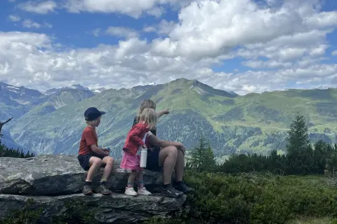 Familj njuter av en fantastisk utsikt under en bad gastein vandring. Barnen pekar ut över de gröna bergen och molnen.