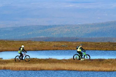 Två cyklister njuter av en cykelsemester i Sverige, susar fram längs sjöar i ett vidsträckt landskap.