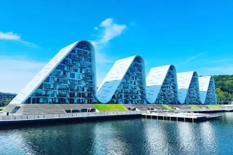 Vågformade byggnader vid vattnet i Vejle, Danmark. Moderna lägenheter med glasfasader och balkonger.
