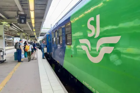 Folk väntar på perrongen vid ett grönt SJ-tåg, redo för en resa. Kanske är det ett tåg till London?