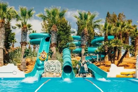 Vattenrutschkanor i Waterworld Ayia Napa med palmer och sol. Två personer åker i en ring nerför en blå vattenrutschkana.