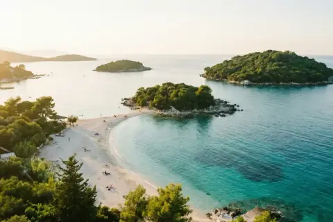 Vacker strand med turkost vatten och gröna öar. Perfekt för en resa till Albanien med tips om sol och bad.