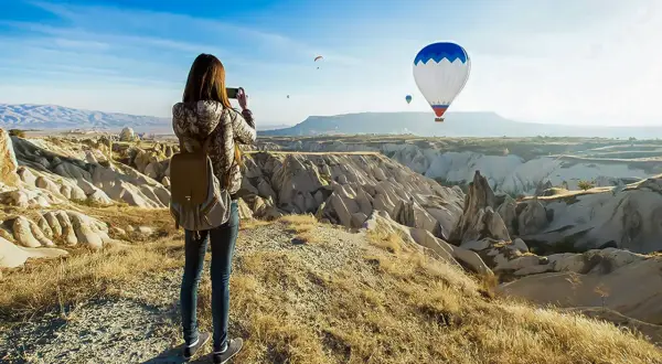 En kvinna med ryggsäck fotograferar den magiska vyn av luftballonger över Kappadokien, Turkiet.