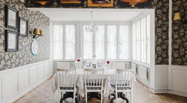 Elegant matsal med dukat bord, blommig tapet och modellbåtar i taket. Perfekt för en middag, som recensionerna för Villa Godthem antyder.