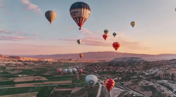 En magisk luftballong tur i Turkiet vid soluppgången. Många färgglada ballonger svävar över ett böljande landskap med byar och klippformationer.