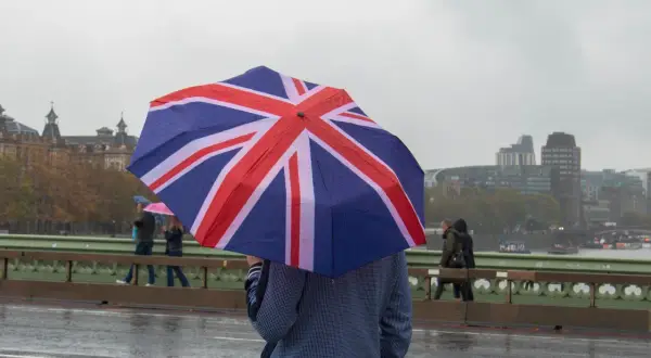 En person med ett paraply med brittiska flaggan på en regnig dag i London. En klassisk vy som visar vad man får inte missa i London.