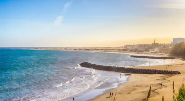 En vidsträckt gran canaria strand med turkost vatten, gyllene sand och några få besökare som njuter av solen.