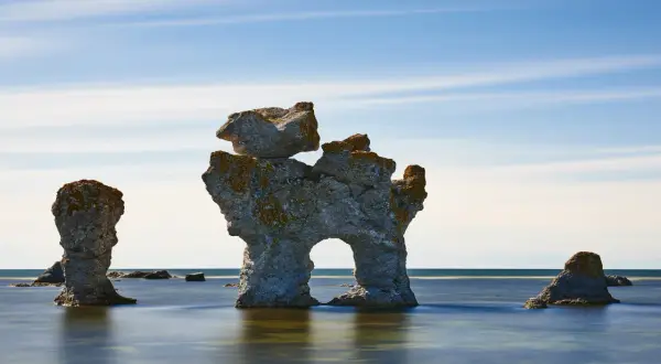Gotlands raukar, mäktiga stenformationer i havet, står som tysta vittnen under en blå himmel med tunna moln.