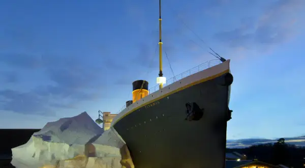 A replica of the Titanic ship is shown at dusk, with an iceberg and the White Star Line building.