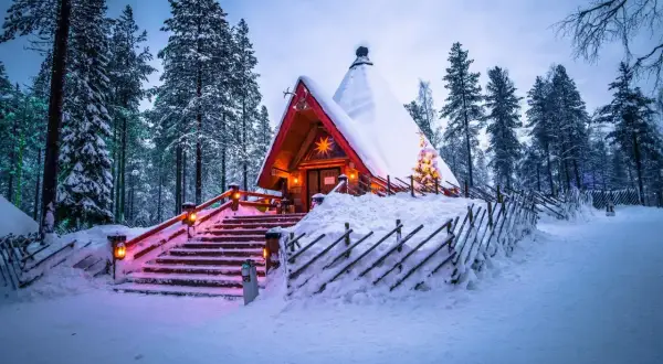 En snötäckt stuga i skogen, upplyst av julbelysning. En dröm för en solsemester vinter.