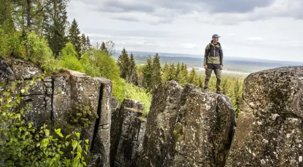 En man står på en klippa och njuter av utsikten över skog och landskap. En perfekt plats för att vandra i Europa.