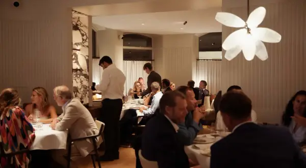 Gäster njuter av en middag på en elegant michelin restaurang i Karlstad. Servitörer serverar mat vid borden.