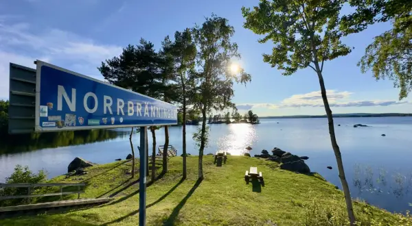 Vacker rastplats vid Norrbränningen, E4 norrut. Solen skiner över sjön, med picknickbord och en brygga.