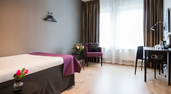 Ett hotellrum med en säng, en lila fåtölj och ett skrivbord. Perfekt för att sova på Arlanda.
