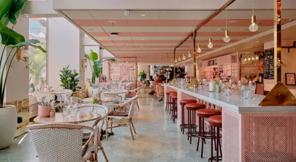 En ljus och luftig lokal med rosa och vita ränder i taket, som påminner om mysiga caféer i Stockholm. Vackra rottingmöbler och mycket gröna växter skapar en inbjudande atmosfär.