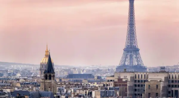 Eiffeltornet höjd över Paris takåsar i rosa skymningsljus. En gyllene kupol syns i bakgrunden.