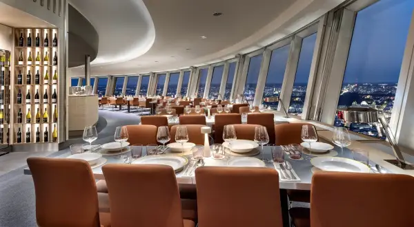 Elegant restaurang Berlin med utsikt över staden. Vackert dukade bord med glas och tallrikar. Vinhylla i bakgrunden.