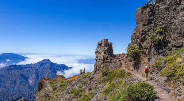 Vandrare på en bergstig med moln och berg i bakgrunden. Fantastiska vandringsleder på Gran Canaria.