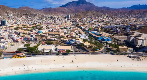 Färgstark stad i Kap Verde med en strand och turkost vatten. Berg reser sig bakom den tätbebyggda staden.