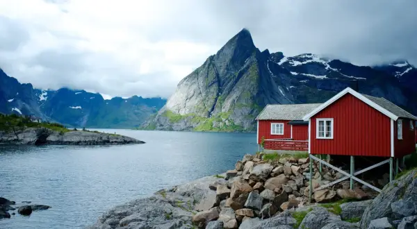 Två röda stugor vid en sjö i Norge, med dramatiska berg i bakgrunden. Perfekt för en vandring i Norge.