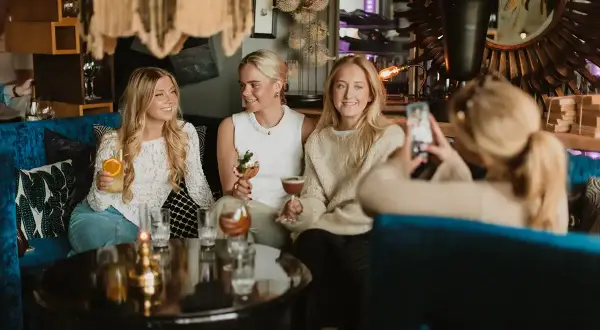 Tre unga kvinnor njuter av drinkar och sällskap under en mysig griffins brunch.
