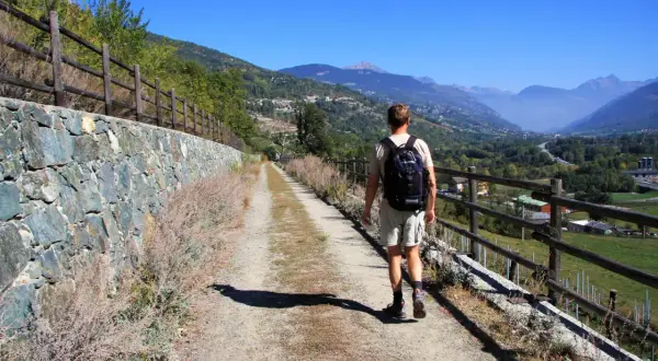 Man vandrar på en grusväg i Italien, med en stenmur till vänster och en vacker dal med berg i bakgrunden.