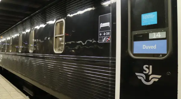 Svart liggvagn SJ vid perrongen. Vagn 14, Duved, med sovande symbol och nummer.