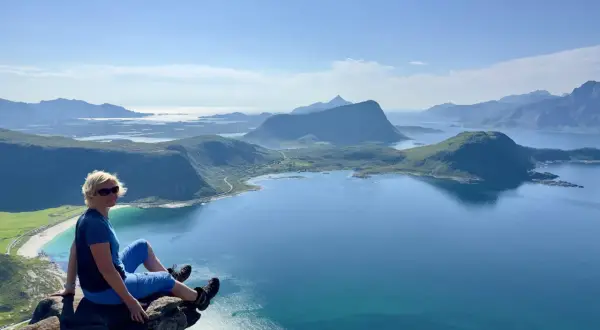 Kvinna sitter på klippavsats med fantastisk utsikt över fjordlandskap på Lofoten.