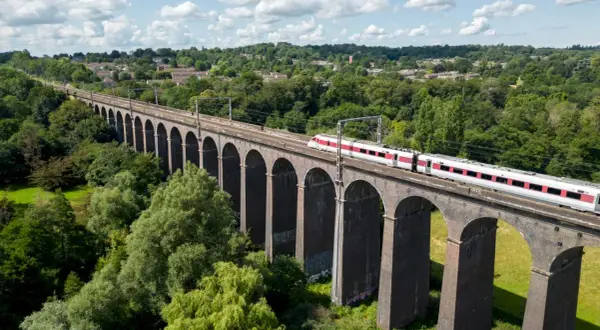 Ett modernt tåg susar fram över en gammal tegelbro, en perfekt bild för att tågluffa i England.