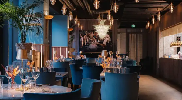 Elegant pava restaurang med blå sammetsstolar, marmorbord och dekorativa lampor.