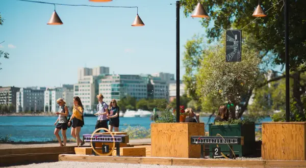 Vänner njuter av utomhusaktiviteter i Stockholm vid vattnet, med spel och stadens silhuett i bakgrunden.