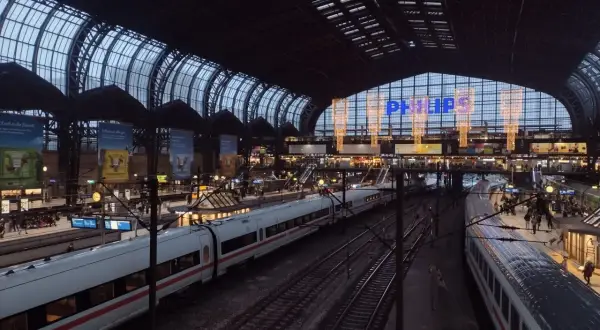 Tågstation med flera spår och vita tåg. En stor glas- och stålkonstruktion täcker taket. Philips-logotypen lyser i blått. Det är ett sj tåg till Hamburg.