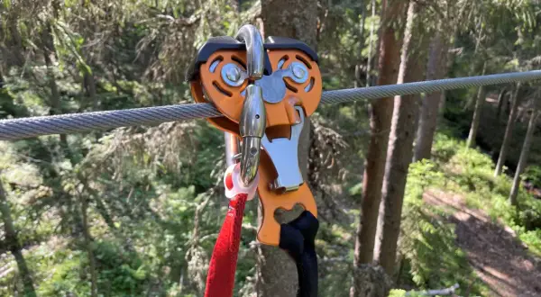 Nära en zipline i Umeå, en orange vajerklämma med röda och svarta band hänger redo för äventyr i skogen.