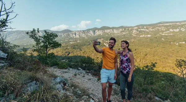 Ett par tar en selfie under sin vandring i Kroatien, med en fantastisk utsikt över berg och grönska.