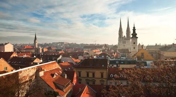 Vy över Zagreb, kroatiens huvudstad, med dess karakteristiska röda tak och imponerande katedral som reser sig mot en molnig himmel.