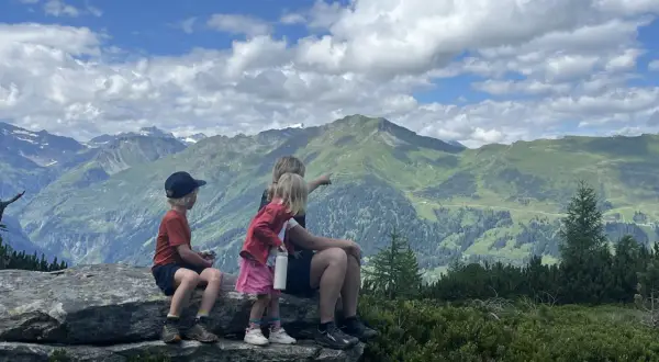 Familj njuter av en fantastisk utsikt under en bad gastein vandring. Barnen pekar ut över de gröna bergen och molnen.