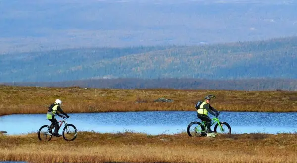 Två cyklister njuter av en cykelsemester i Sverige, susar fram längs sjöar i ett vidsträckt landskap.