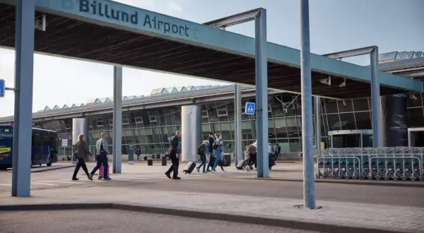 Människor med resväskor korsar vägen vid Billund Airport, redo att flyga till Legoland.