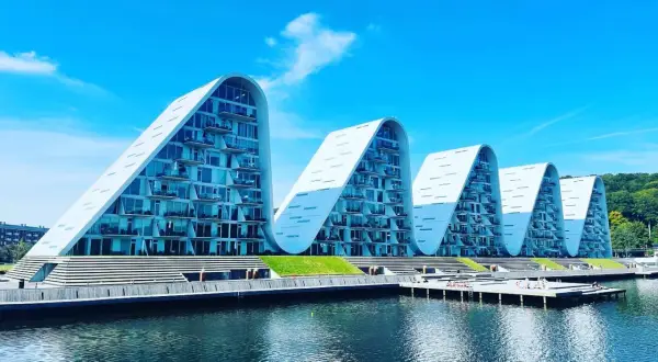 Vågformade byggnader vid vattnet i Vejle, Danmark. Moderna lägenheter med glasfasader och balkonger.