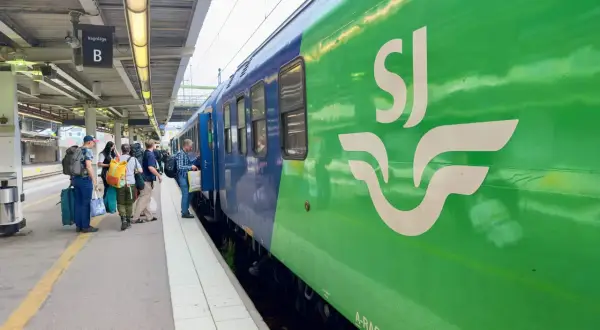 Folk väntar på perrongen vid ett grönt SJ-tåg, redo för en resa. Kanske är det ett tåg till London?