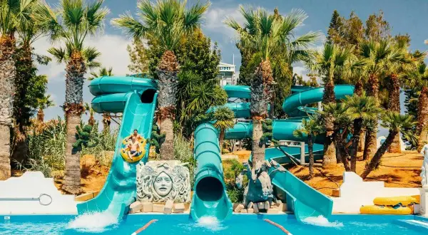 Vattenrutschkanor i Waterworld Ayia Napa med palmer och sol. Två personer åker i en ring nerför en blå vattenrutschkana.