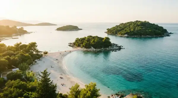 Vacker strand med turkost vatten och gröna öar. Perfekt för en resa till Albanien med tips om sol och bad.