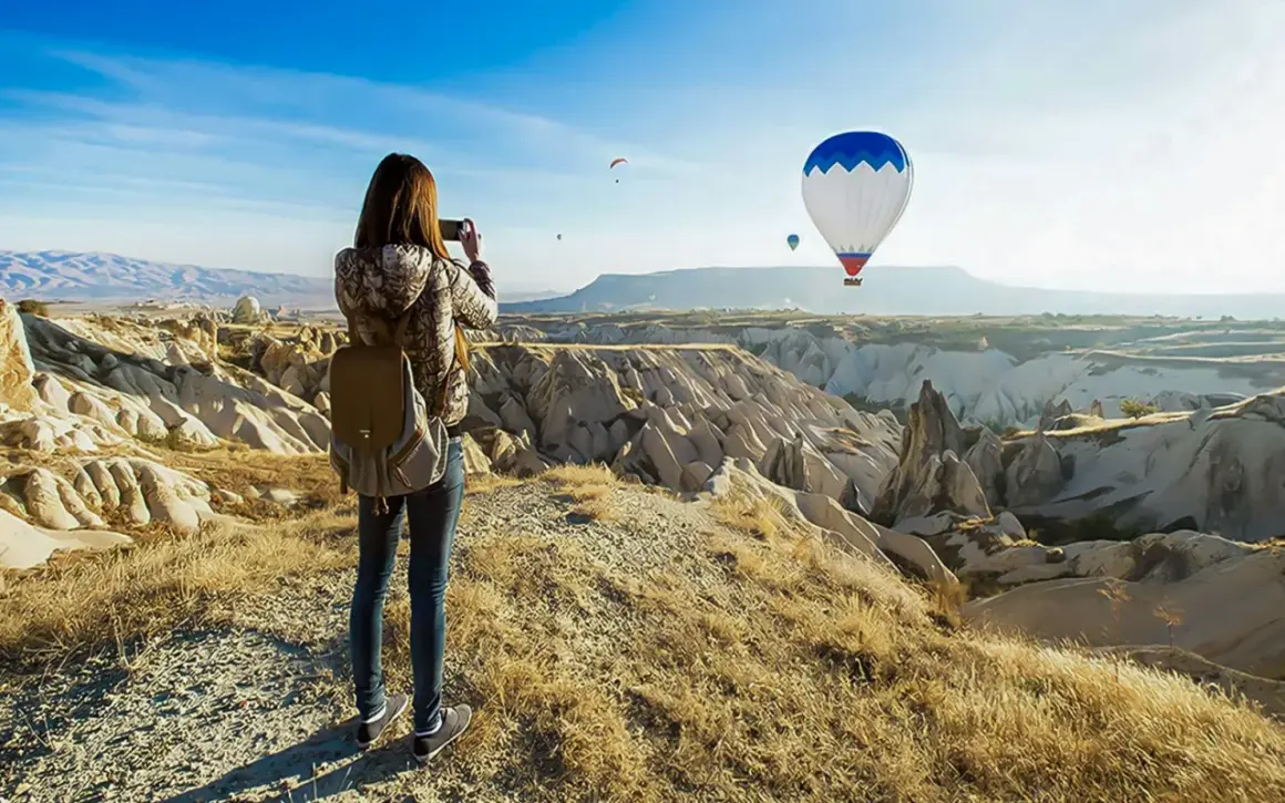 En kvinna med ryggsäck fotograferar den magiska vyn av luftballonger över Kappadokien, Turkiet.