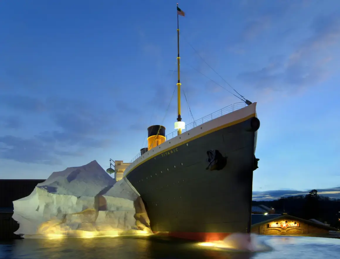 A replica of the Titanic ship is shown at dusk, with an iceberg and the White Star Line building.